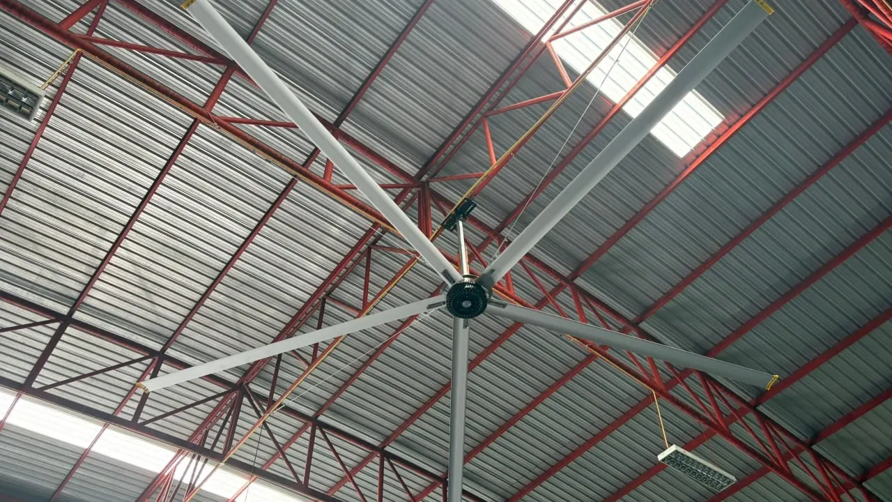 พัดลมยักษ์ HVLS Mactech ติดตั้งใต้หลังคาโครงถักเหล็กสีแดงของโกดัง