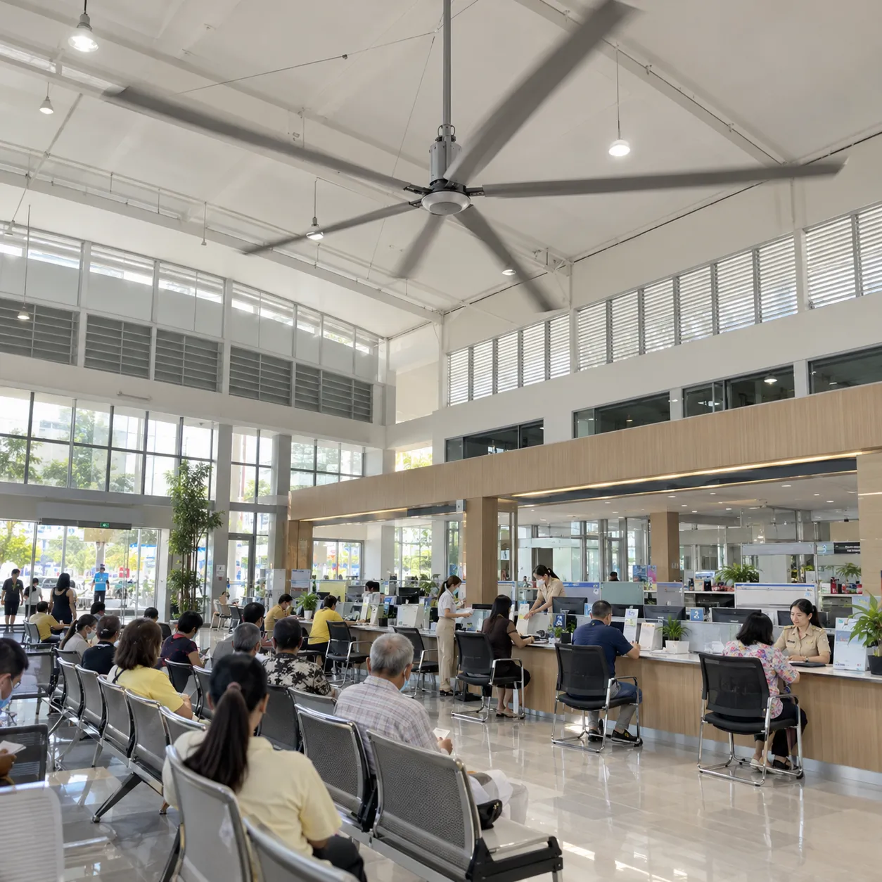 พัดลมยักษ์ HVLS ใต้หลังคาห้องโถงบริการประชาชนของหน่วยงานราชการ ประชาชนนั่งรอรับบริการหน้าเคาน์เตอร์