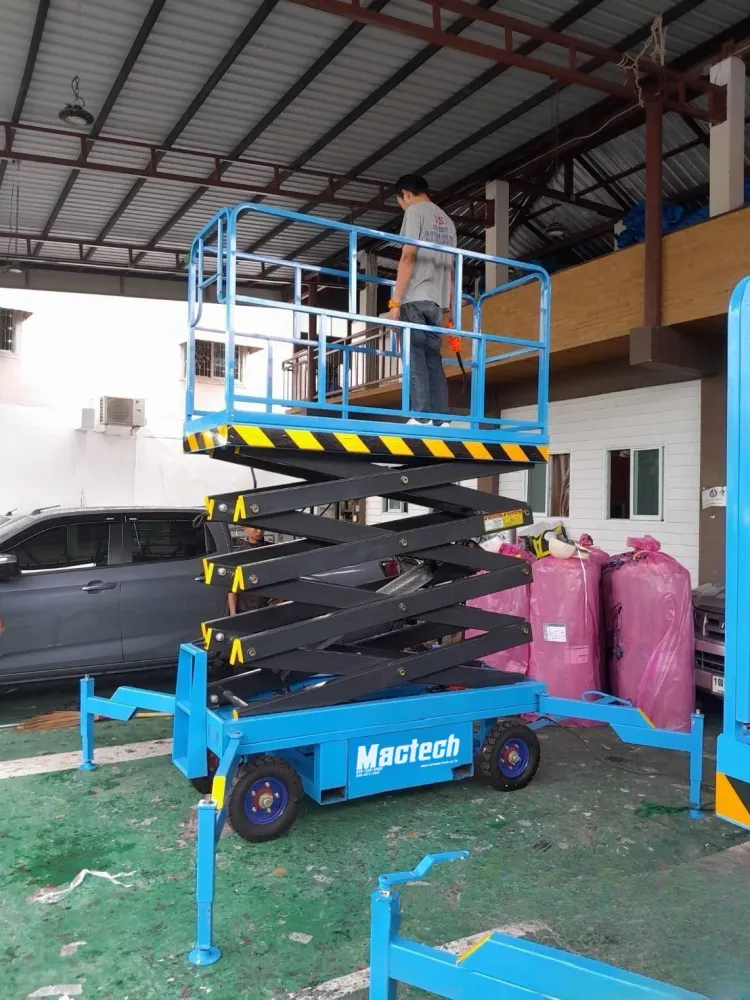 รถกระเช้ากรรไกร Mactech รุ่นเข็นสีฟ้า กางขาค้ำยันและยกแท่นทำงานหน้าอาคาร