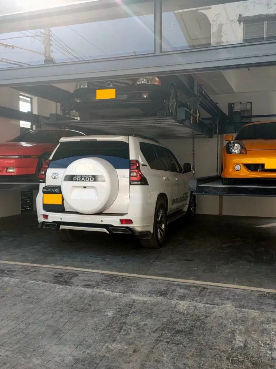 รถ SUV สีขาวจอดใต้แท่นลิฟท์จอดรถ 6 คัน Mactech ที่ยกรถอีกคันขึ้นด้านบน