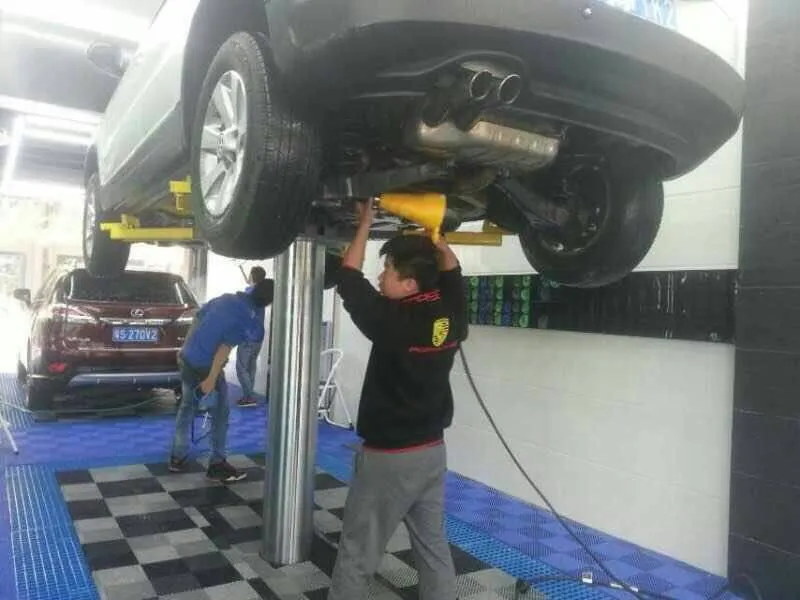 พนักงานทำงานใต้ท้องรถที่ยกบนลิฟท์เสาเดียวในร้านคาร์แคร์