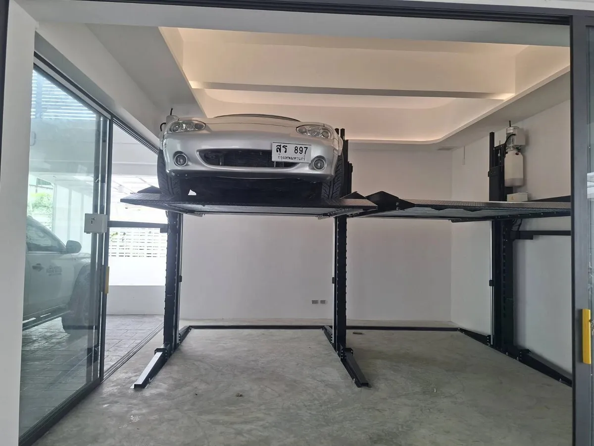 ลิฟท์จอดรถ 2 เสาในโรงรถกระจก รถเก๋งสีเงินอยู่บนแท่นที่ยกขึ้น